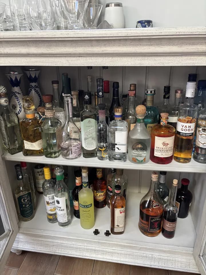 Top shelves of the white cabinet: tequila decanters, gin, flavored vodka, limoncello and Fireball